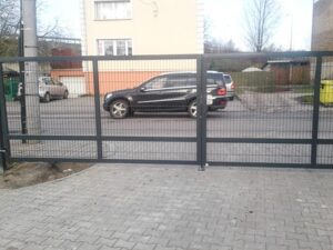 Einfahrt mit parkenden Autos und Gitterzaun.