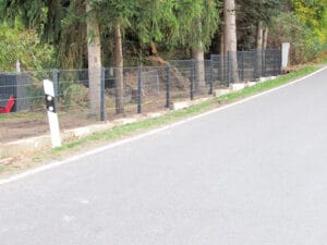 Straße mit Absperrzaun und Bäumen im Hintergrund.