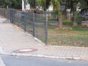 Gepflasterter Gehweg mit Metallzaun und Gartengrundstück.
