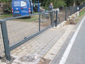 Bauarbeiter bei Zauninstallation neben gepflastertem Weg.