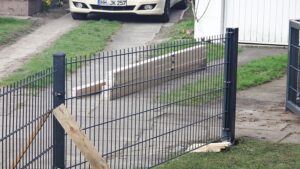 Metallzaun, kaputtes Tor, geparkter Lieferwagen.