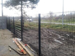 Gitterzaun an einer Straße mit Bauholz.