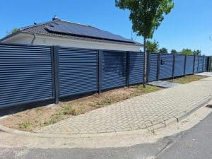 Langer, moderner Metallzaun mit Lamellen und integrierter Pforte – hergestellt von Komabud Zaune in Polen.