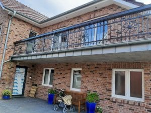 Ziegelhaus mit Balkon und Kinderwagen vor Tür.