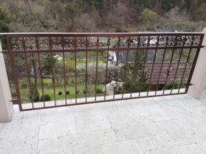 Schmiedeeisernes Geländer an Terrasse mit Gartenblick.