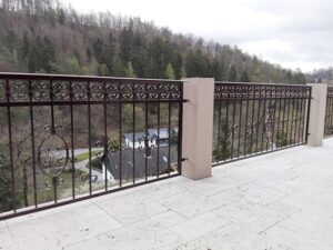 Blick von dekorativem Geländer auf Wald und Gebäude.