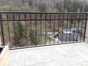 Verziertes Balkongeländer mit Waldansicht.