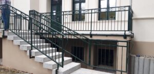 Außentreppe mit grünem Geländer und Steinplatten.