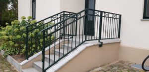 Grüne Eisengeländer an Außentreppe mit Granitstufen.