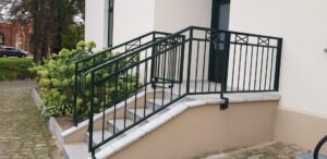 Außentreppe mit grünem Geländer und Pflanzen.