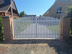 Modernes weißes Gartentor mit Rundbogenprofil, montiert zwischen zwei gemauerten Ziegelpfosten – elegante und zeitlose Lösung für Einfahrten.