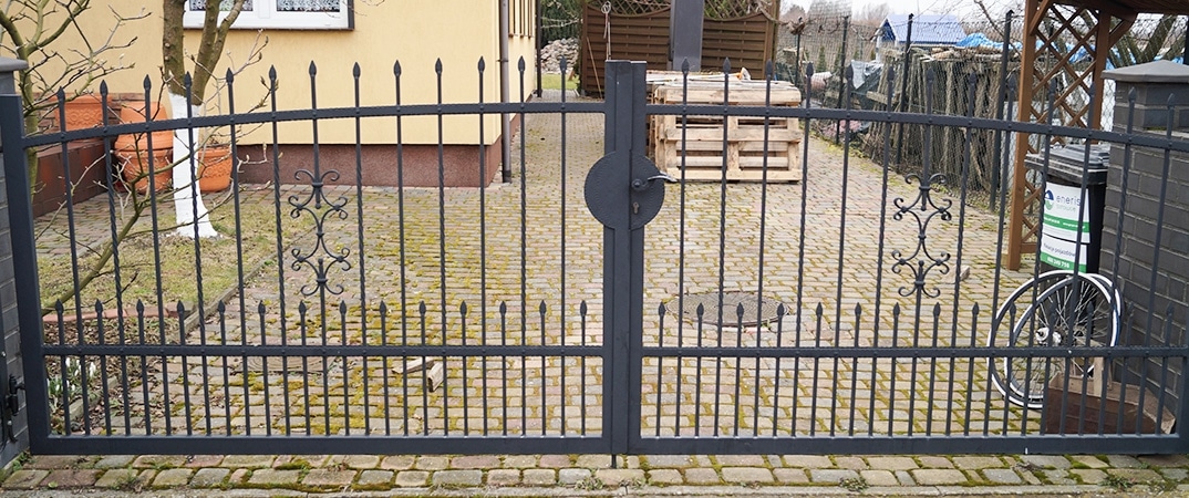 Metallgartentor mit Verzierungen vor Pflastersteinweg.