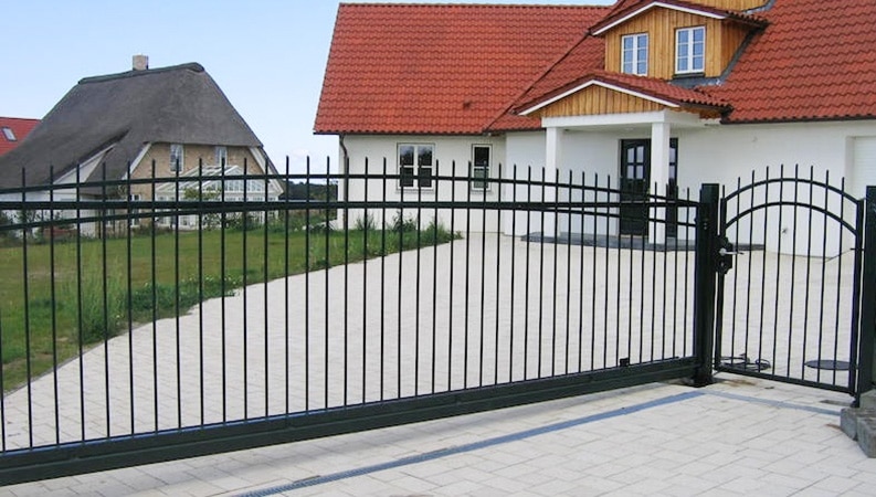 Einfahrtstor vor Einfamilienhaus mit Reetdachhaus im Hintergrund.