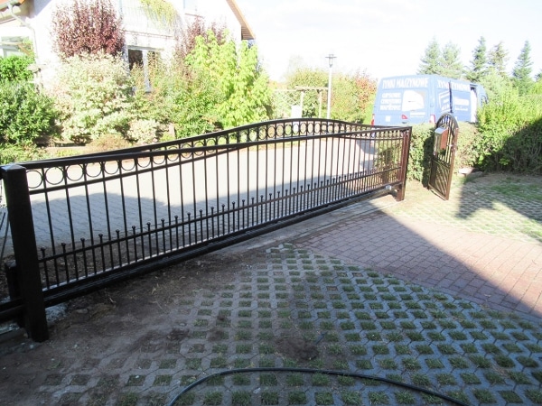 Schmiedeeisernes Gartentor mit Einfahrt und Pflastersteinen.