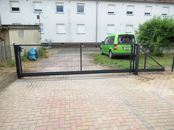 Metalltor vor Wohnblock mit grünem Auto.