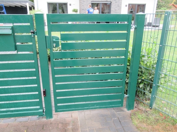 Grünes Gartentor mit zwei Personen im Hintergrund.