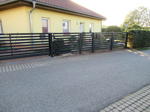Moderne Einfahrt mit schwarzem Zaun und Pflastersteinen.