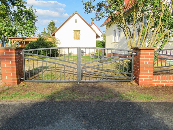 Einfahrtstor vor ländlichem Haus und Garten.