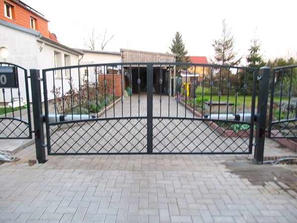 Geschlossenes Gartentor vor Gehweg und Gebäude.