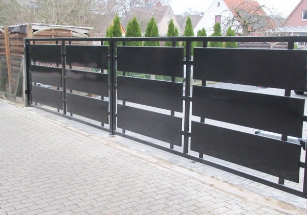 Schwarzes Metalltor vor Einfahrt und Hecke.