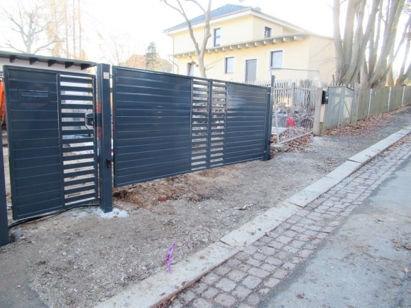 Moderner Einfahrtstor und Zaun an einer Straße.