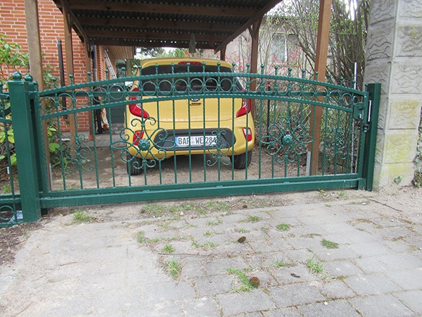Gelbes Auto hinter grünem schmiedeeisernen Tor.