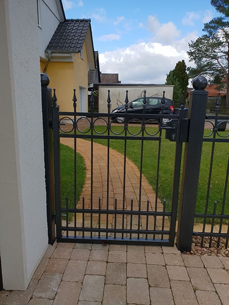 Hauseingang mit geschlossenem Metalltor und Gartenweg.