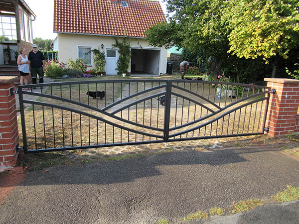Einfahrt mit Metalltor und Personen im Hintergrund
