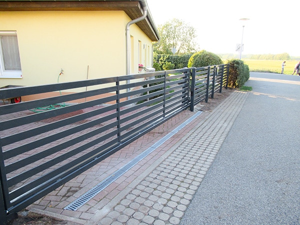 Metallzaun am Haus mit Gehweg und Grünfläche.