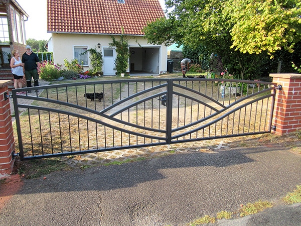 Einfahrtstor aus Metall vor Einfamilienhaus mit Personen.