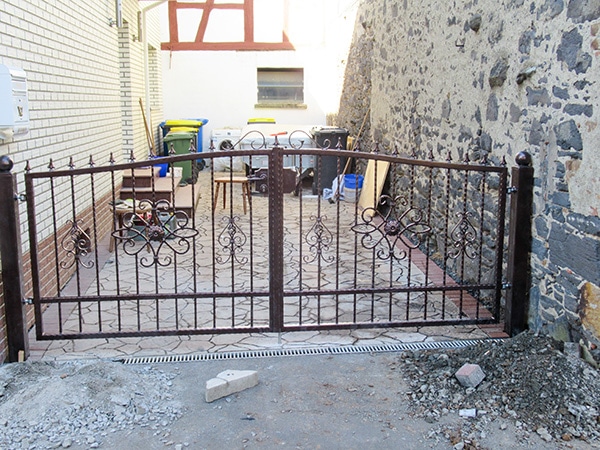 Verziertes Eisentor vor einem Innenhof.