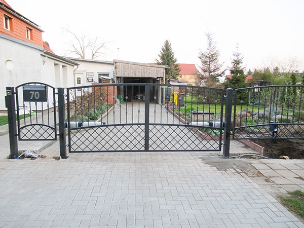 Metalltor Einfahrt mit Pflastersteinen und Gartenansicht.