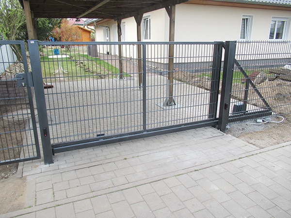 Schwarzes Gartentor aus Metall, Einfahrt mit Pflastersteinen.