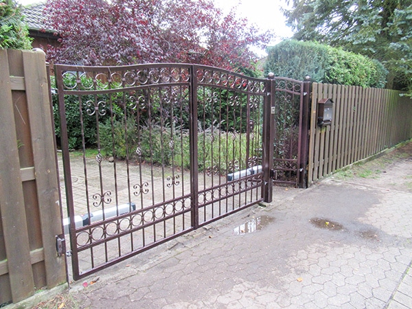 Verschnörkeltes Eisentor und Holzzaun am Einfahrtsweg.