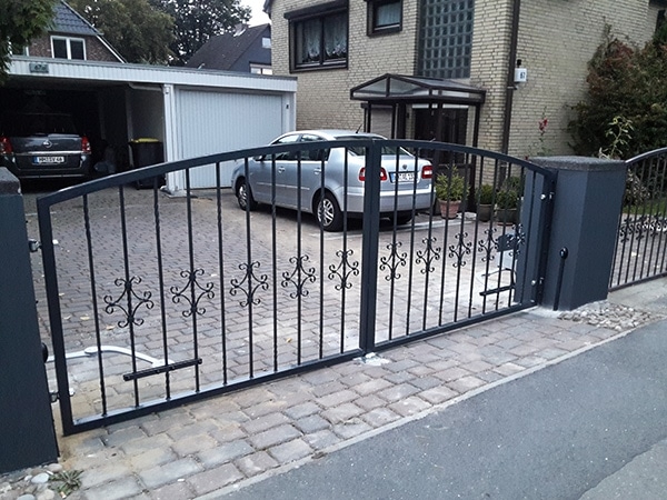 Schmiedeeisernes Gartentor vor Einfahrt mit Auto.