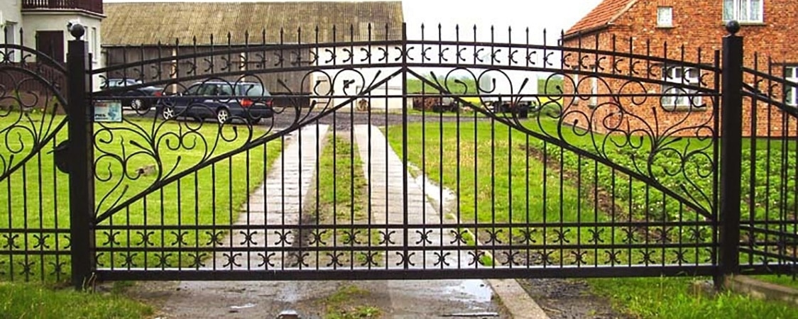 Verschnörkeltes Eisentor vor einem ländlichen Anwesen.