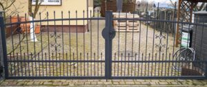 Metallgartentor mit Verzierungen vor Pflastersteinweg.