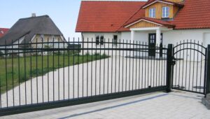 Einfahrtstor vor Einfamilienhaus mit Reetdachhaus im Hintergrund.