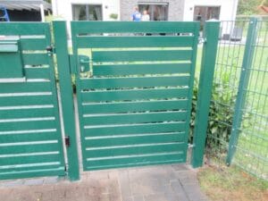 Grünes Gartentor mit zwei Personen im Hintergrund.