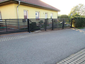 Moderne Einfahrt mit schwarzem Zaun und Pflastersteinen.