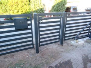 Schwarzes Gartentor mit Briefkasten und Hecke.