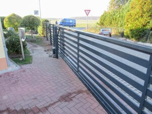 Pflasterweg mit Metallzaun und Straßenschildern.