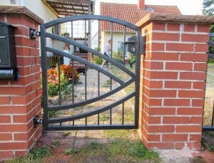 Metallgittertor mit Ziegelsteinsäulen und Person im Hintergrund