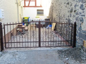 Eisentor vor einem Hinterhof mit Mülltonnen.