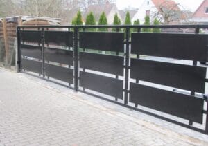 Schwarzes Metalltor vor Einfahrt und Hecke.