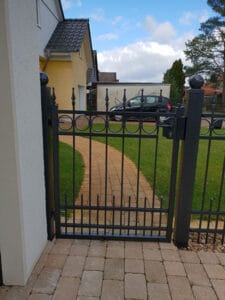 Hauseingang mit geschlossenem Metalltor und Gartenweg.