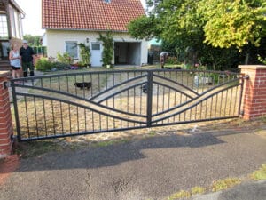 Einfahrtstor aus Metall vor Einfamilienhaus mit Personen.