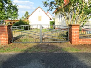 Zweiflügeliges Metalltor vor Einfamilienhaus im Sonnenlicht.