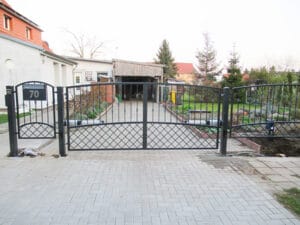 Metalltor Einfahrt mit Pflastersteinen und Gartenansicht.