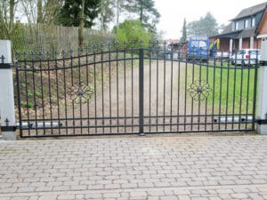 Schmiedeeisernes Tor mit Dekorelementen und Pflastersteinweg.